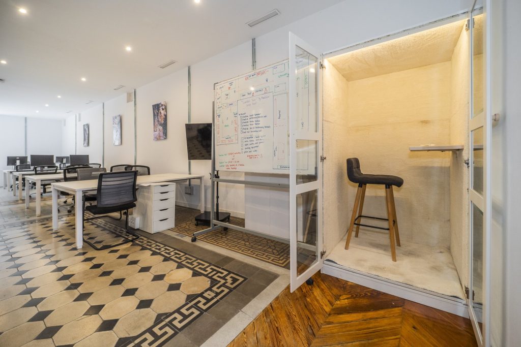 Oficina de startup con una cabina telefónica para llamadas privadas y una pizarra para asegurar la continuidad operativa durante el traslado.