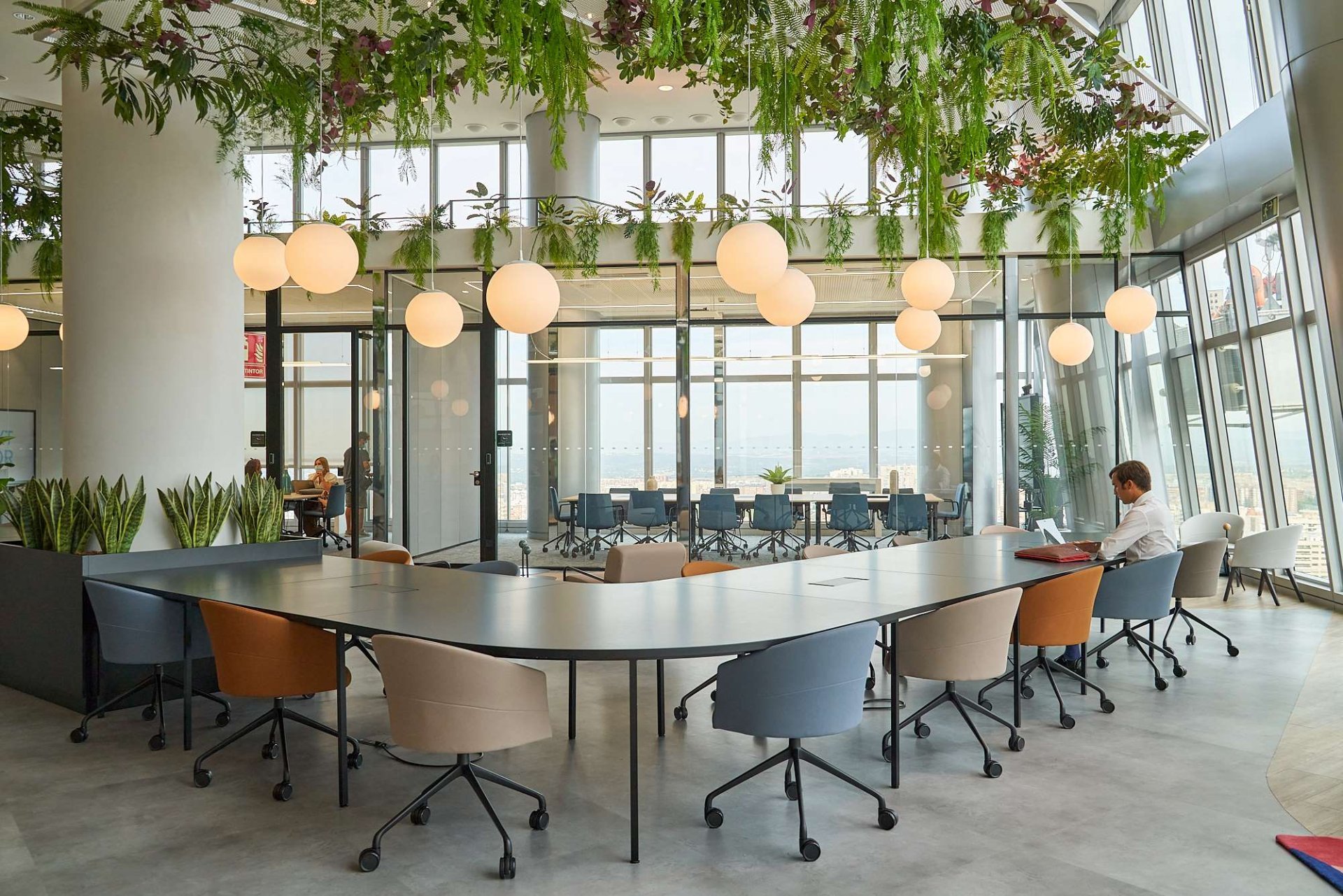 Oficina moderna con alto wellbeing, mostrando un diseño biofílico con plantas colgantes y grandes ventanas con luz natural para la retención de talento.