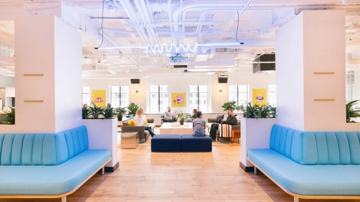 Zonas comunes modernas con sofás azules y neones en WeWork Paseo de Gracia, ideal para startups que buscan imagen de marca premium.