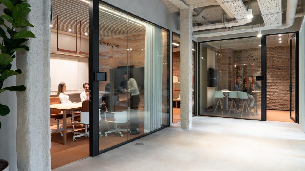 Equipos colaborando en salas de reunión de cristal, un pilar del ROI de la oficina que fomenta la productividad y la innovación.