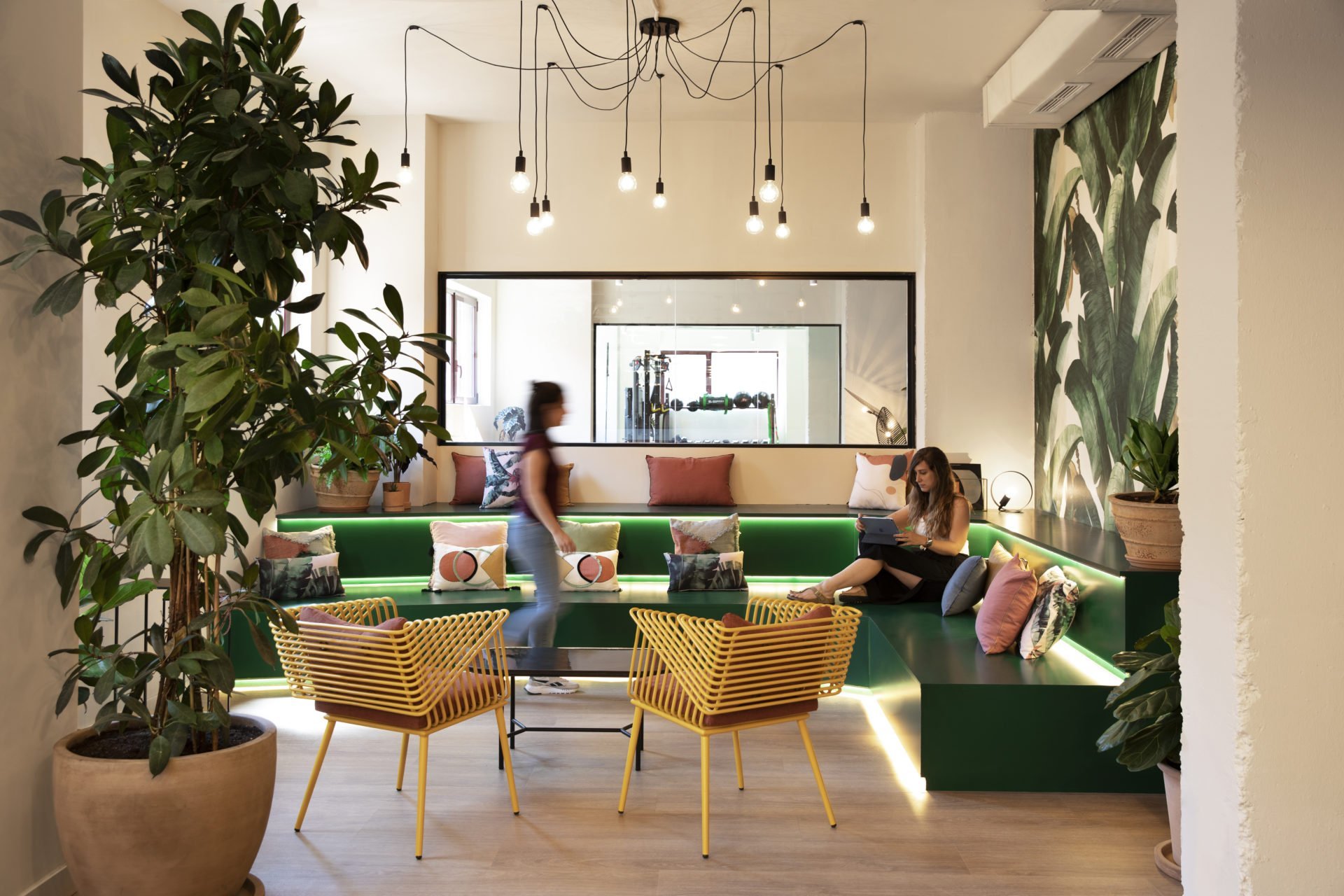 Zona lounge moderna en oficina para startups con diseño biofílico y espacios de reunión informal para fomentar la retención de talento.