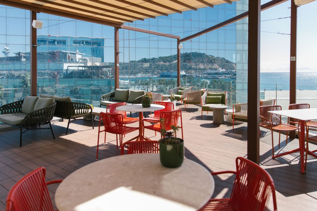 Terraza exterior de una oficina con vistas al mar y mobiliario colorido, representando el workplace wellbeing y la retención de talento en startups.