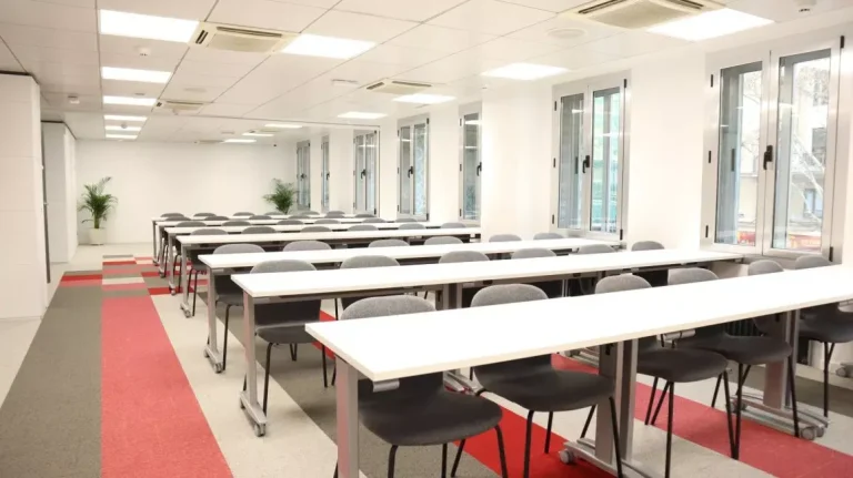 Amplia sala de formación con filas de mesas blancas en Cink Ríos Rosas, un espacio versátil para reuniones de equipos en crecimiento.