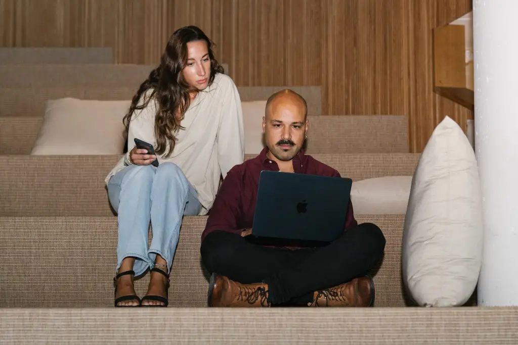 Dos empleados de una startup trabajando con un ordenador portátil en unas gradas de madera informales, reflejando una cultura de empresa colaborativa y horizontal.