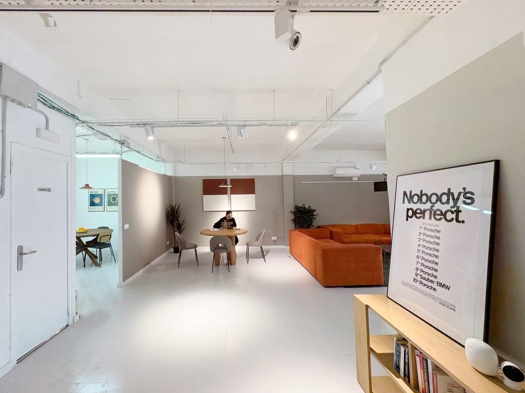 Espacio de oficina flexible con un sofá naranja vibrante y áreas de reunión abiertas, que ilustra cómo el diseño de oficina de marca fomenta la identidad corporativa.