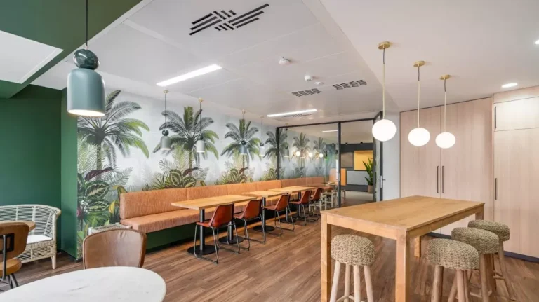 Zona de comedor y café en Utopicus Diagonal con mesas de madera y papel pintado tropical, un entorno innovador para los descansos.