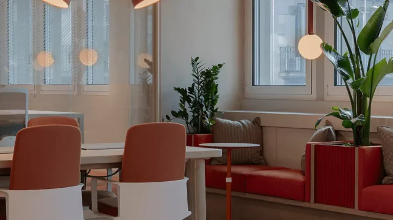 Rincón de descanso confortable con sofás rojos, plantas naturales y grandes ventanales en NN Pau Claris Barcelona.