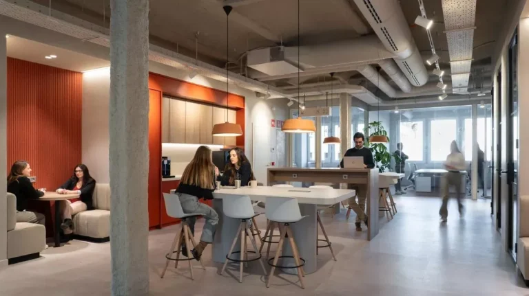 Área de cocina colaborativa con mesas altas y taburetes de diseño para fomentar el networking en el centro NN Pau Claris.