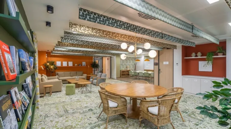 Área de descanso y comunidad en el coworking Utopicus Diagonal con sillones, plantas y estanterías de libros, fomentando el networking orgánico.